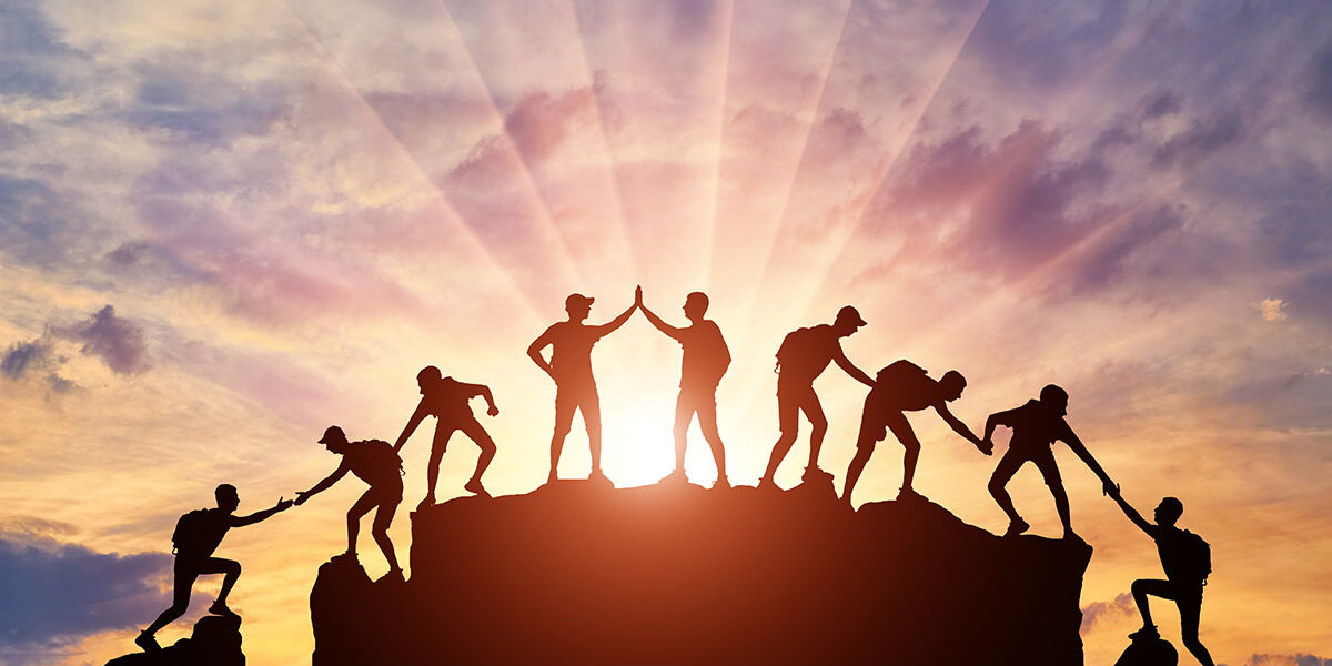 WeGo Groupin rekrytointiblogissa käytetty kansikuva. Kuvassa näkyy vuorelle kiipeäviä ihmisiä, jotka toimivat yheisvoimin. Taustalla paistaa iltaaurinko ja värimaailma on auringonlaskua kuvaava.