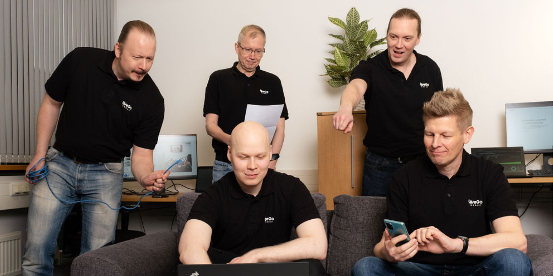 Wegon it-palvelut ja it-ulkoistuspalvelut tiimi tietokoneen ympärillä. Taustalla on useita eri it-laitteita kuen tietokoneita ja näyttöjä.
