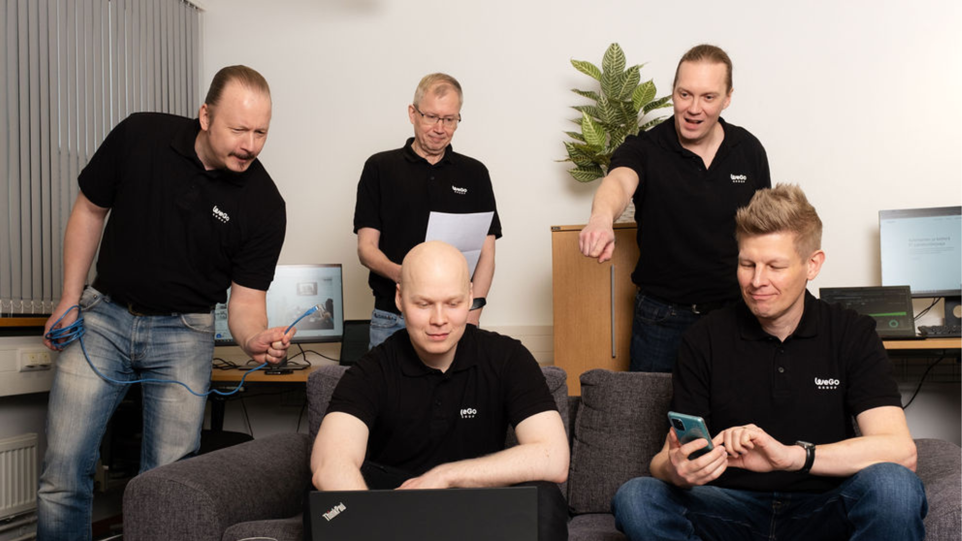 Wegon it-palvelut ja it-ulkoistuspalvelut tiimi tietokoneen ympärillä. Taustalla on useita eri it-laitteita kuen tietokoneita ja näyttöjä.